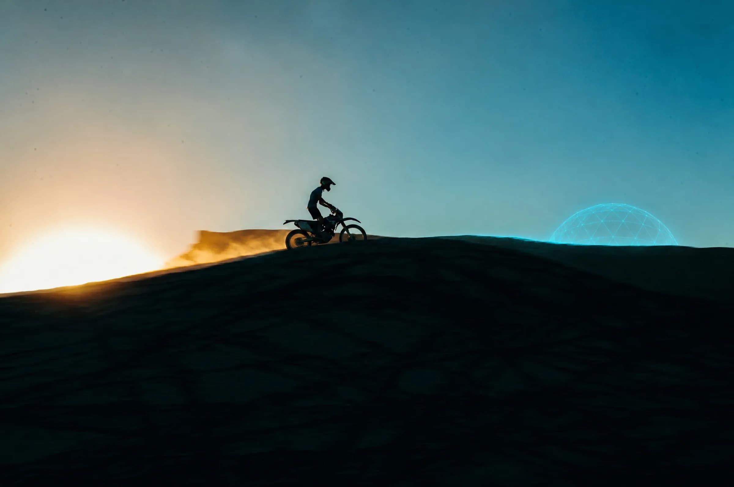 Motocross-Fahrer als Silhouette auf einer Düne im Abendlicht, dahinter eine leuchtende Netz-Kuppel